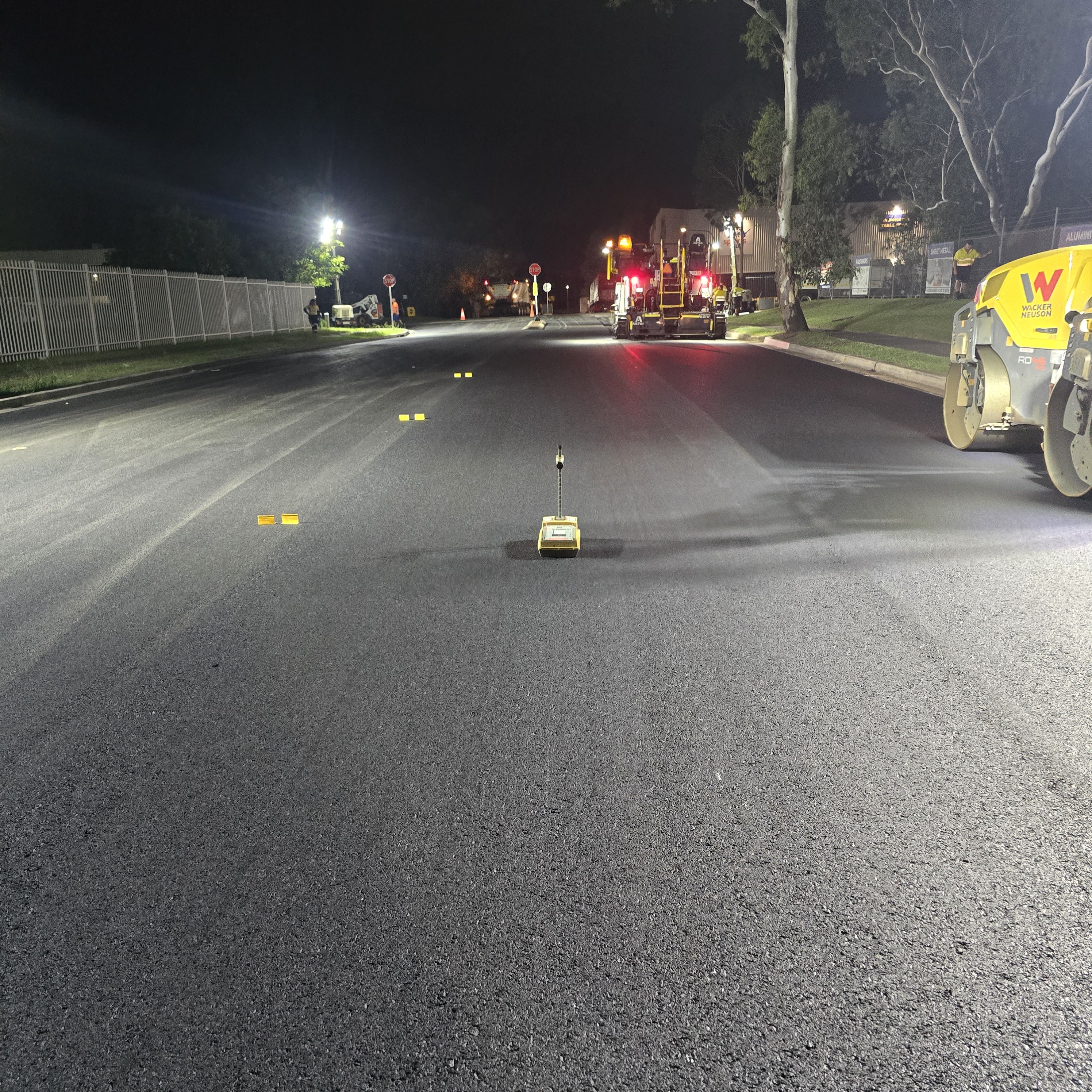 Nuclear density gauge placed on asphalt during night paving operation with roller in background